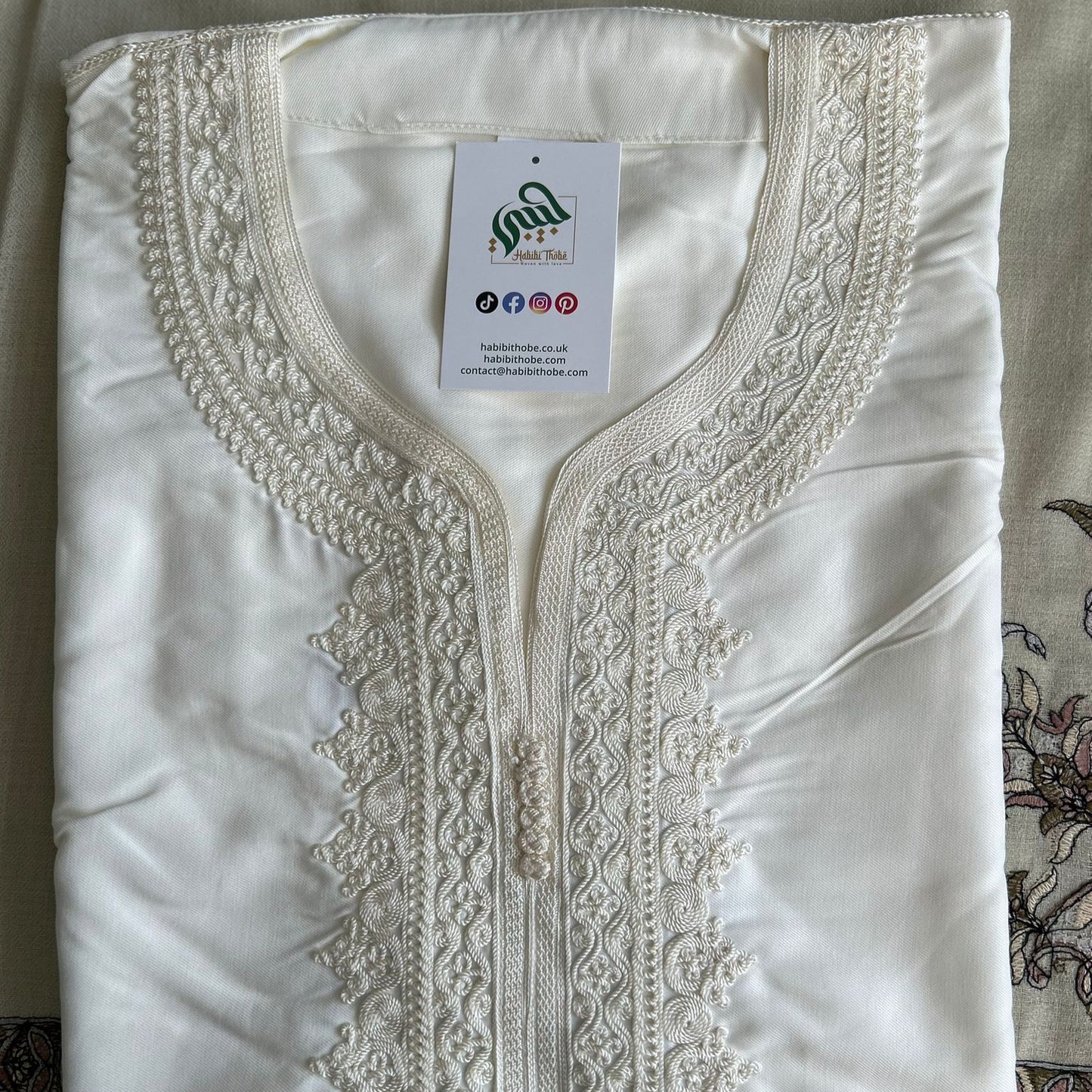 “White Moroccan Gandoura with detailed cream embroidery and central tassel, showcasing refined craftsmanship.”