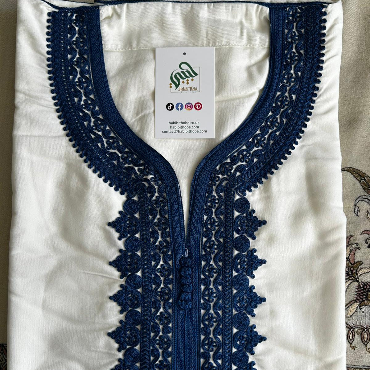 “White Moroccan Gandoura featuring deep navy embroidery around the neckline and chest, traditional and elegant.”