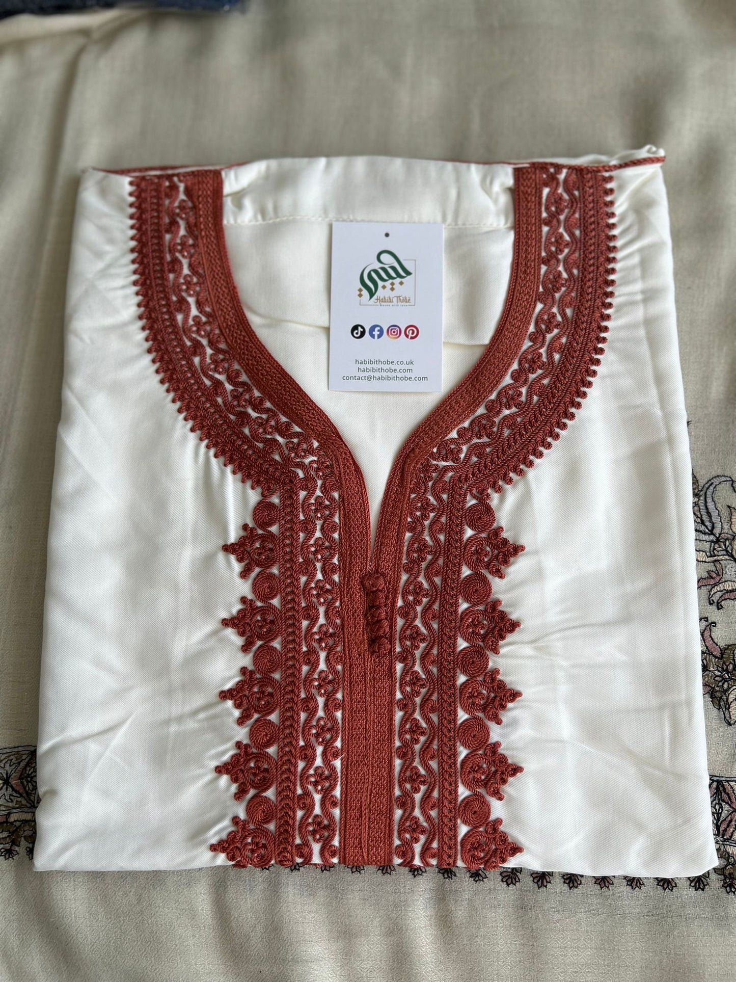 “White Moroccan Gandoura with detailed orange embroidery and central tassel, showcasing refined craftsmanship.”
