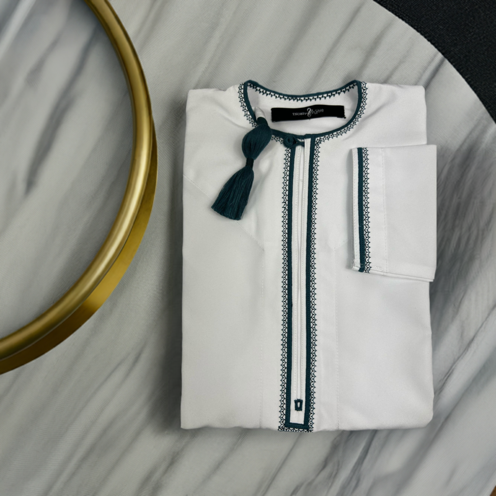 "Omani white thobe with emerald green tassels, folded, showcasing elegant craftsmanship and traditional design."