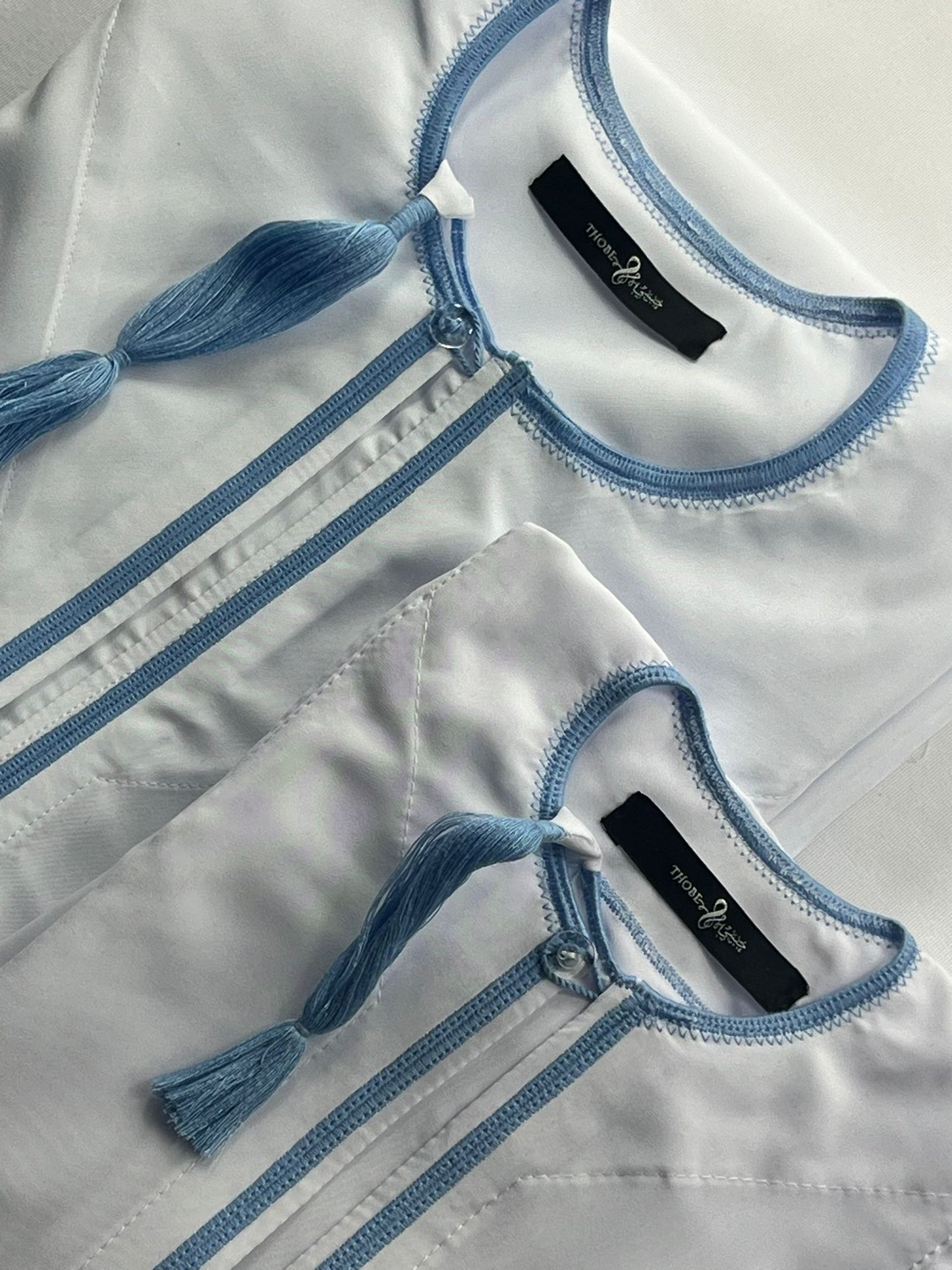 "Close-up of Mikhael white and sky blue father and son thobes, highlighting the intricate design and matching accents for a coordinated look."