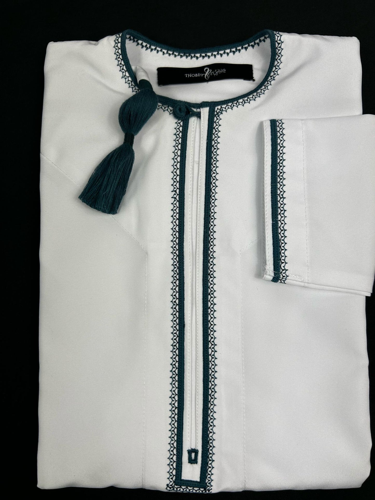 "Folded Mikhael white and emerald green father and son thobes, showcasing detailed sleeve design and coordinated traditional style."