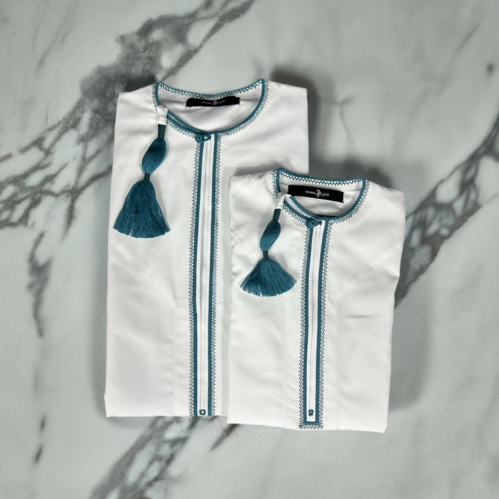 "Father and son matching Mikhael white thobes with emerald green accents, elegantly folded, showcasing traditional style and coordinated design."