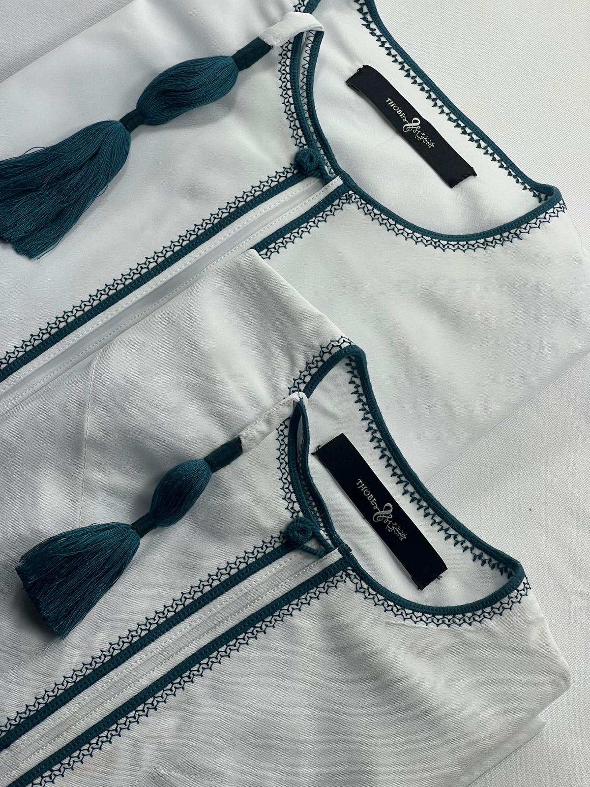 "Close-up of Mikhael white and emerald green father and son thobes, highlighting the intricate design and matching accents for a coordinated look."