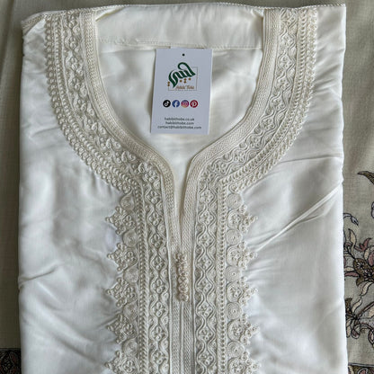 “White Moroccan Gandoura with detailed cream embroidery and central tassel, showcasing refined craftsmanship.”