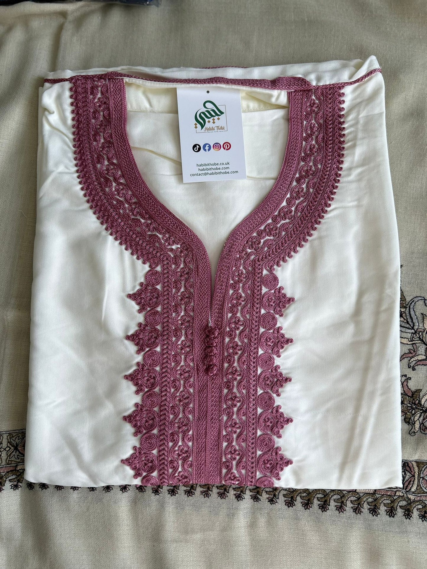  “White Moroccan Gandoura with detailed pink embroidery and central buttons , showcasing refined craftsmanship.”