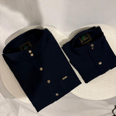 Two navy blue shirts with gold buttons on a white woven surface